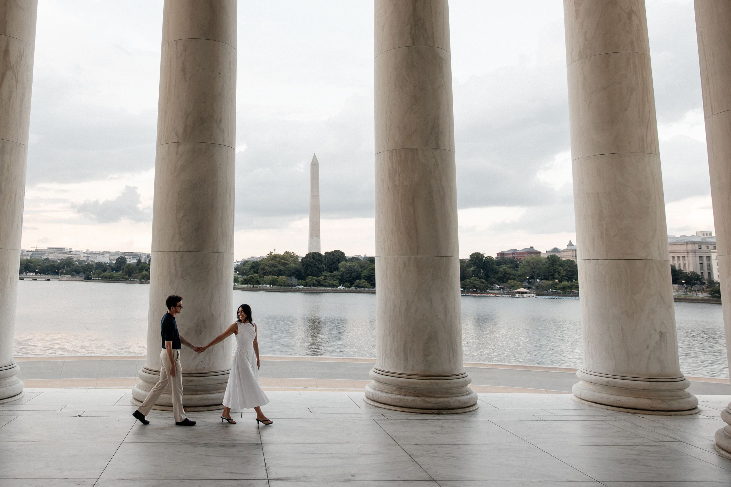 Joseph and Filiz walking hand in hand between the marble columns of the Jefferson Memorial, the Washington Monument across the water behind them